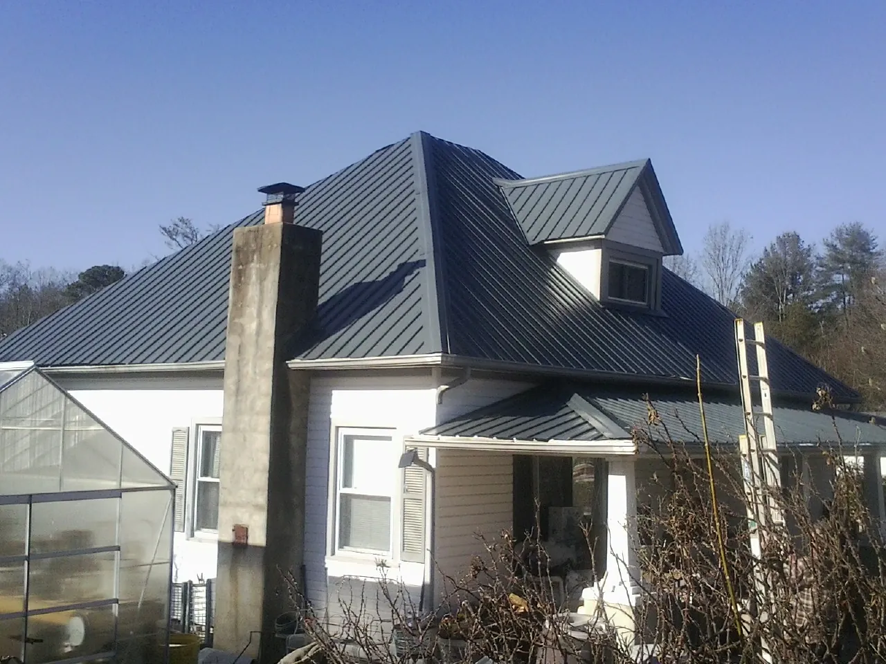 Dark blue standing seam metal roof on a white farmhouse with dormer — Slate & Tile Roof Repair by Roofing Brothers in Melrose