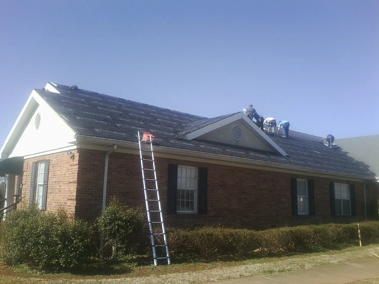 Crew tearing shingles off a brick ranch roof with a ladder set — Metal Roof Repair work by our crew in Melrose