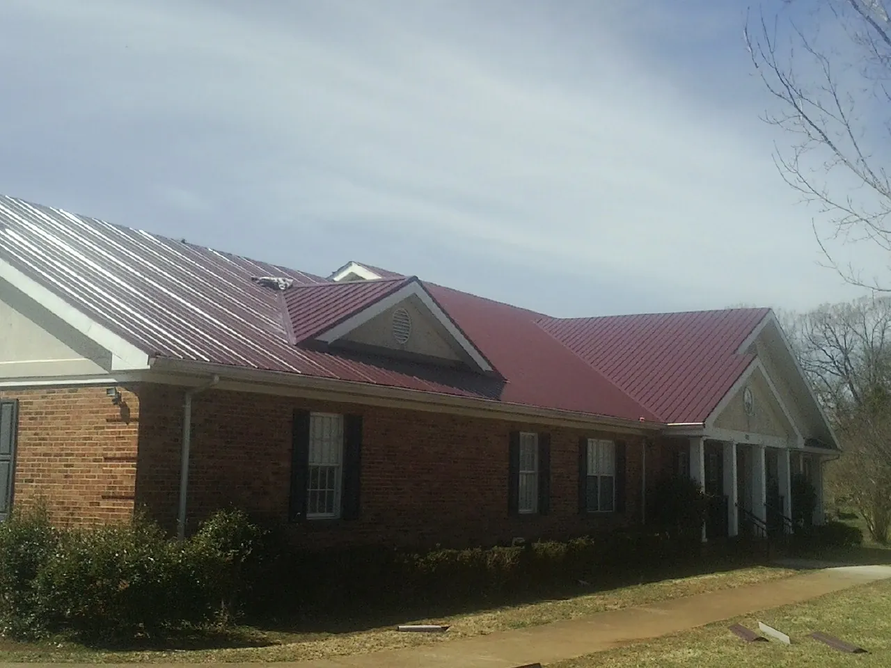 Red metal roof with gabled entries on a long brick building, from a Hail Damage Roof Repair job in Melrose